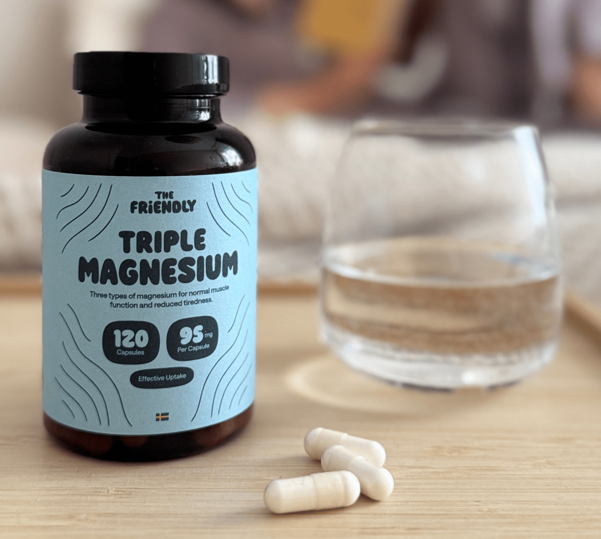 Bottle of Triple Magnesium on a table with a glass of water and three magnesium capsules.