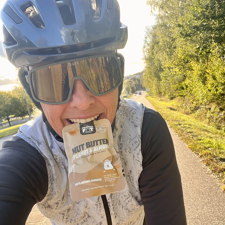 Woman cycling with a Nut Butter Peanut & Almond snack pack between her teeth.